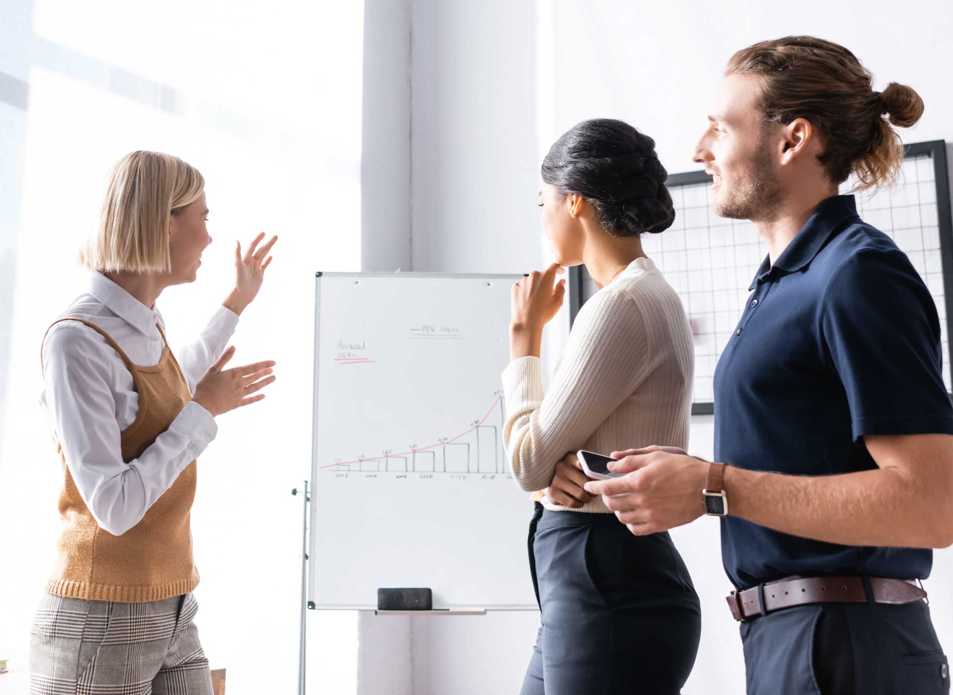 3 people standing in discussion around a whiteboard